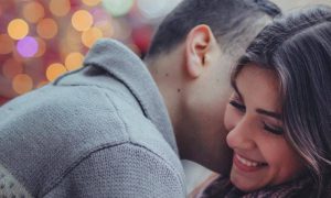 man kisses girlfriend on neck while girl happily smiles