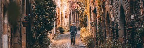 elderly man hand in pocket walks alone along footpath between old buildings