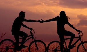 couple shadow rides two bikes hand in hand in beautiful sunset