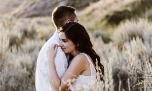 couple stands on field hugging in sunny sky