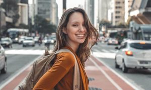 woman stands on footpath on crowded street happily smiling