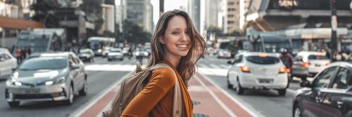 woman stands on footpath on crowded street happily smiling