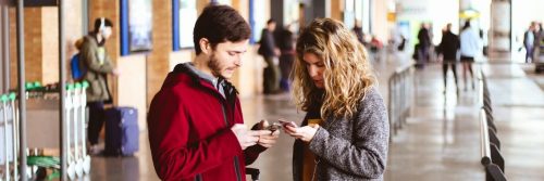 couple stands in airport checking mobile phone