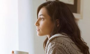 woman sits alone in silent room drinking coffee looking through window