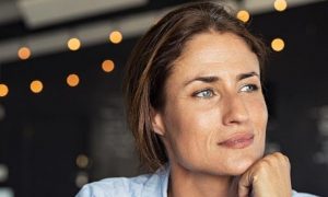 woman hand over chin sits in coffee shop thinking