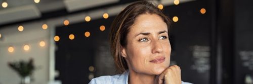 woman hand over chin sits in coffee shop thinking