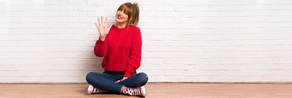 woman sits leg crossed hi 5 happily smiling next to white stone wall