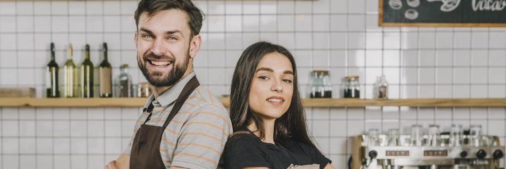 bartender couple standing back to back smiling in coffee shop