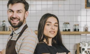 bartender couple standing back to back smiling in coffee shop