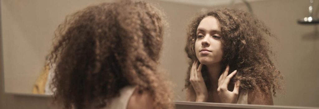 long curly hair girl looks herself in mirror