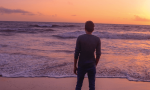 man facing backward stands hand in pocket on beach in beautiful sunset sky
