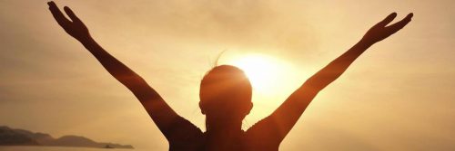 woman raises hands feeling grateful in sunny sky