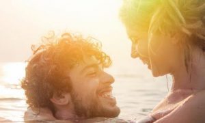 couple happily swims on beach looking smiling at each other in sunny sky