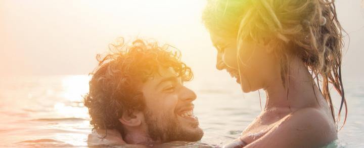 couple happily swims on beach looking smiling at each other in sunny sky