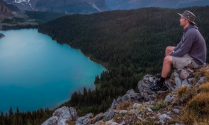 man sits on rock on top of mountain beside lake