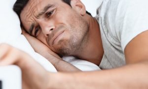 man lies on bed holding clock having insomnia problem