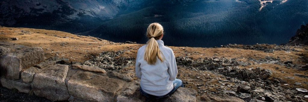 woman sits on rock facing backward focuses on breathing immersing into nature