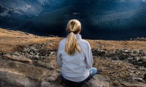 woman sits on rock facing backward focuses on breathing immersing into nature