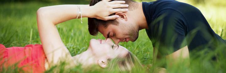 woman lies on field about to kiss boyfriend while man sitting head to head with her