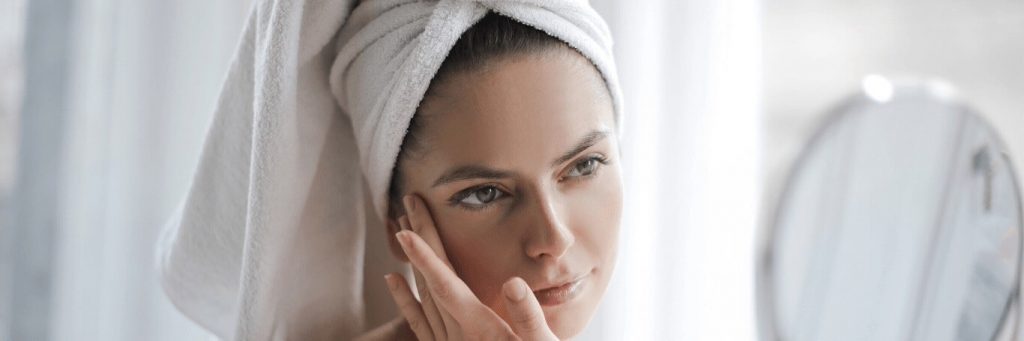 woman covering hair with white towel applies skin care