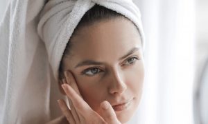 woman covering hair with white towel applies skin care