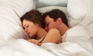 couple sleeps tightly on bed beside side table