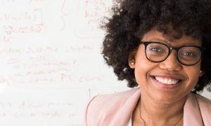 curly hair woman with black frame glass happily stands beside whiteboard with mathematics functions smiling