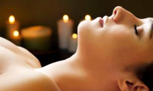 woman lies down eyes closed covering body with towel beside candles