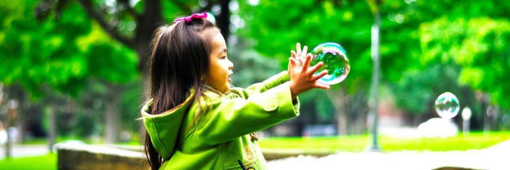 adorable girl wearing green coat happily excitedly plays with bubbles in park