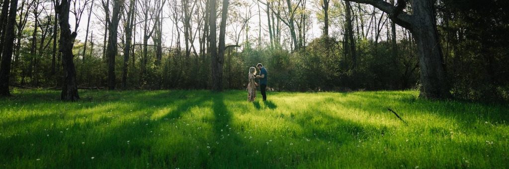 couple stands on green grass forest talking