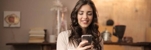 woman happily smiles using mobile phone for online learning in tidy living room
