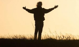 man stands facing backward on field gratitude life in red clear sky