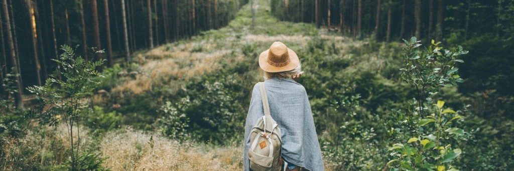 woman wearing back bag facing backward stands in forest