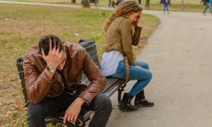 couple sits on bench in park head on face having conflict not talking to each other