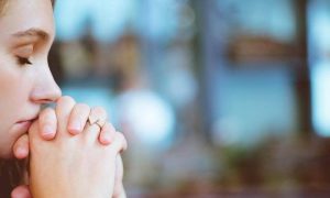 woman eyes closed sits holding hands thinking praying