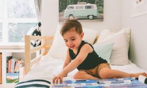 little adorable boy sits on bed excitedly read kids children book in tidy cozy bedroom