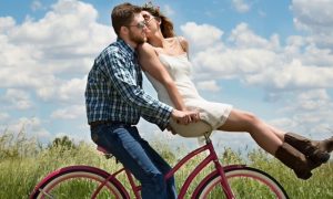 couple happily ride along green field while woman sits in front kissing partner