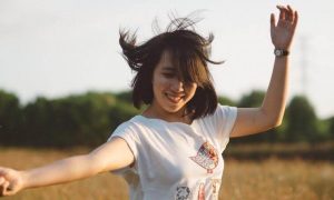 short hair woman dances on field happily smiling carrying flowers in clear sky