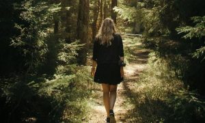 woman facing backward walks alone in forest