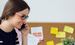 woman happily smiles answering phone while sitting in office