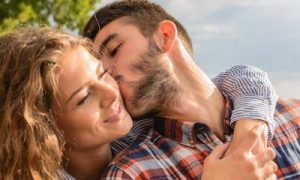 man kisses girlfriend on cheek while woman hugging from behind