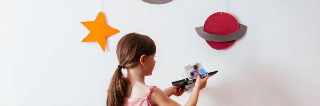 little girl plays toy beside white wall decorated with universe symbols