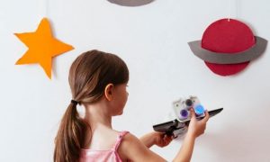 little girl plays toy beside white wall decorated with universe symbols
