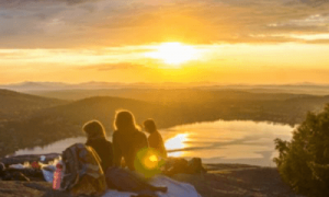 group of people sits on mountain top enjoying picnic watching sunset