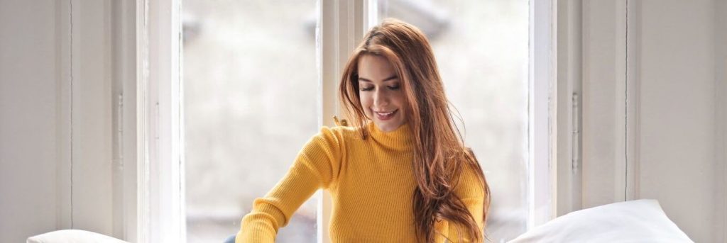 woman sits beside window in bed happily smiling