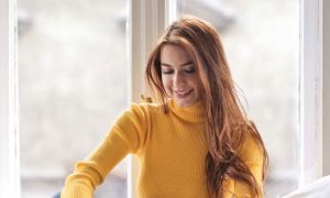 woman sits beside window in bed happily smiling