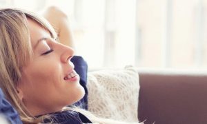 woman hands over head lying on couch smiling