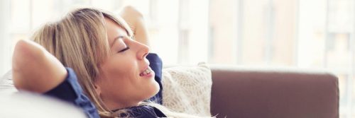 woman hands over head lying on couch smiling