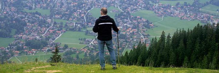 elderly stands on mountain top holding stick looking at countryside