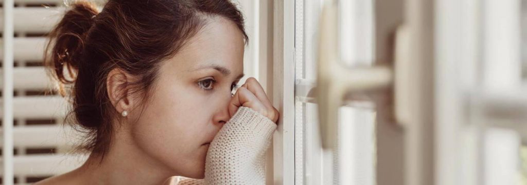 woman stand hand in face beside window feeling sad due to betrayal